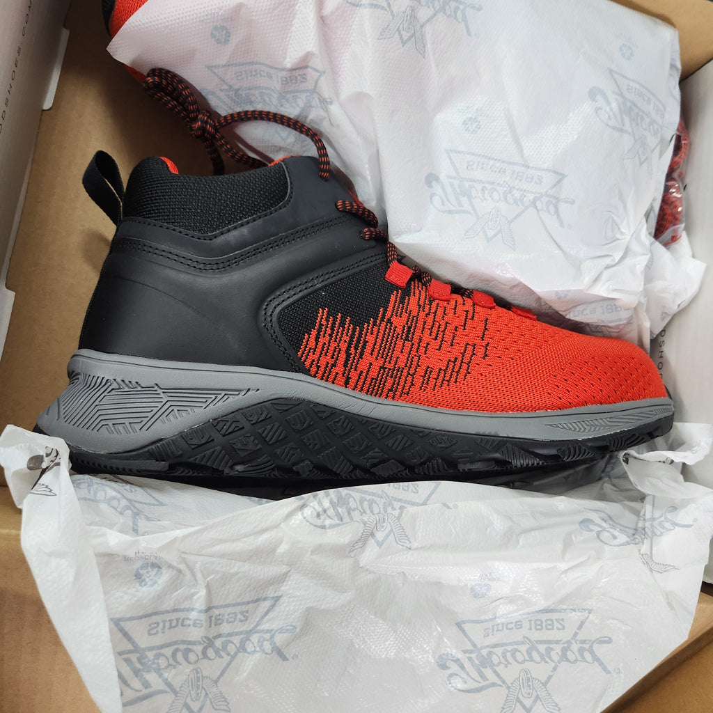 A single high-top sneaker shown inside its box, surrounded by branded white tissue paper. The shoe has a black leather and mesh upper with a bright orange-red knit pattern on the side, a gray midsole, and black laces.